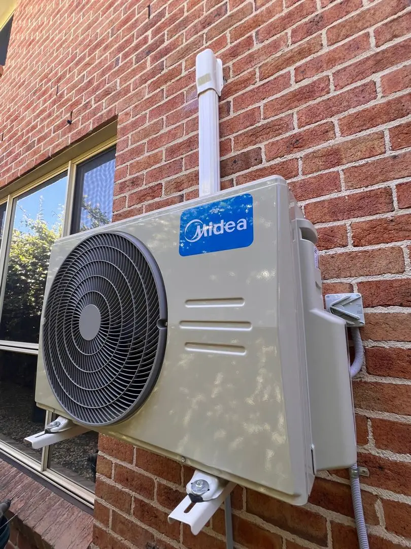 Outdoor condenser bracket-mounted on a brick wall with a straight, clipped conduit run.